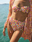 A girl wearing the GORGONIA BIKINI, showcasing its vibrant pattern, on a wooden deck overlooking the beach