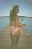 A girl wearing the GORGONIA BIKINI, showcasing its vibrant pattern, on a wooden deck overlooking the beach