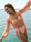 A girl wearing the GORGONIA BIKINI, showcasing its vibrant pattern, on a wooden deck overlooking the beach